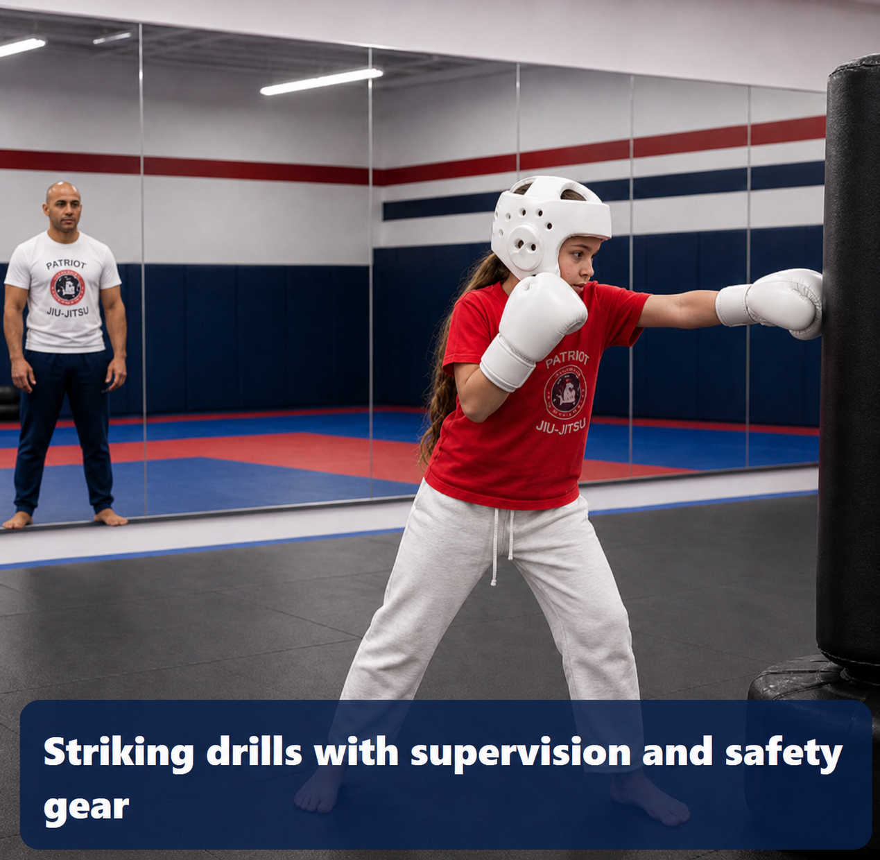 Young girl wearing gloves, headgear, and a red Patriot Jiu-jitsu shirt hitting a punching bag beside a mirror wall while a tan trainer watches from the background